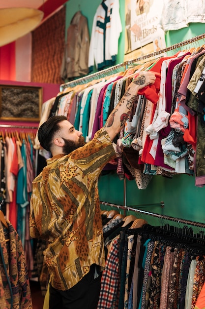 Jeune homme barbu choisissant un t-shirt rouge dans la boutique de vêtements