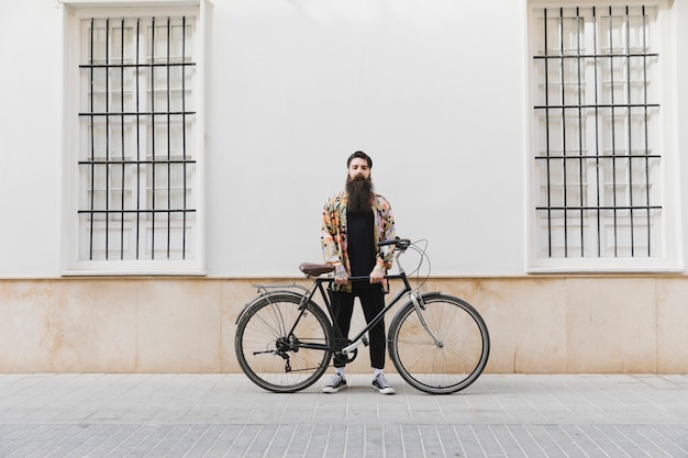 Jeune homme barbu debout avec vélo contre mur