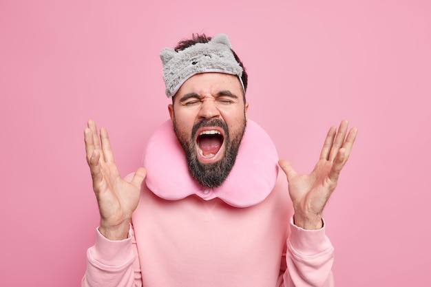 Photo gratuite un jeune homme barbu émotionnel crie fort garde la bouche grande ouverte les gestes voyagent activement sur de longues distances en voiture porte un oreiller de voyage autour du cou