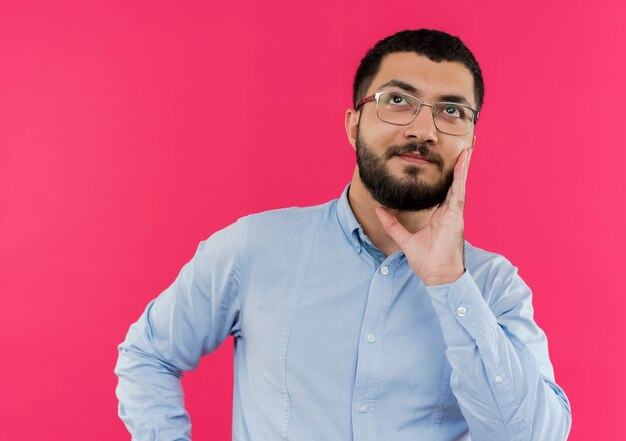 Jeune homme barbu à lunettes et chemise bleue à la perplexité