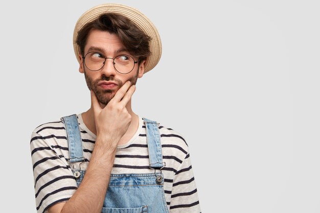 Jeune homme barbu avec des lunettes rondes et une salopette en denim