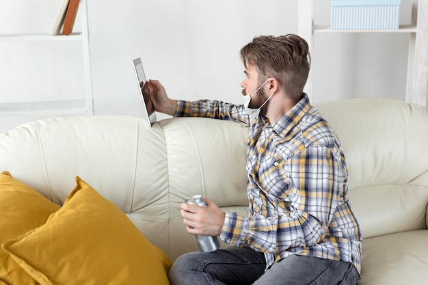 Jeune homme barbu parcourant la tablette sur le canapé