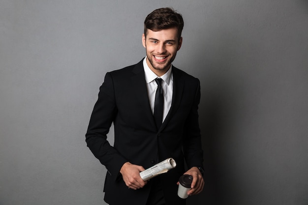 Jeune homme barbu souriant en tenue de soirée tenant un journal et une tasse de café,