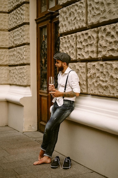 Jeune homme barbu tatoué. Un mec romantique en chemise blanche, casquette et bretelles se promène dans la ville. s'articule autour d'un lampadaire. Peaky Blinders. démodé, rétro.