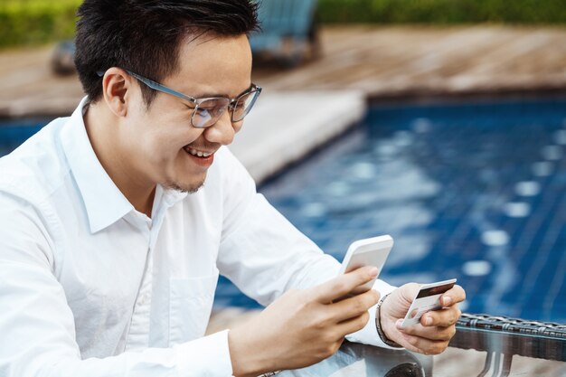 Le jeune homme beau aime faire des achats en ligne sur un téléphone mobile avec une carte de crédit.