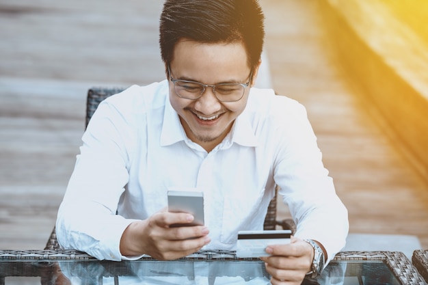 Le jeune homme beau apprécie faire des achats en ligne sur un téléphone mobile avec une carte de crédit.