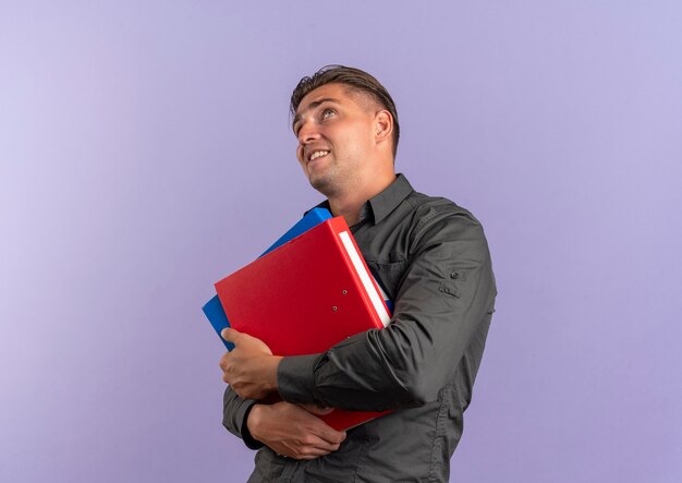 Jeune homme beau blond anxieux détient des dossiers de fichiers et lève les yeux isolé sur l'espace violet avec copie espace