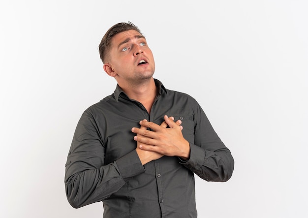 Jeune homme beau blond choqué met les mains dans la poitrine isolé sur fond blanc avec copie espace