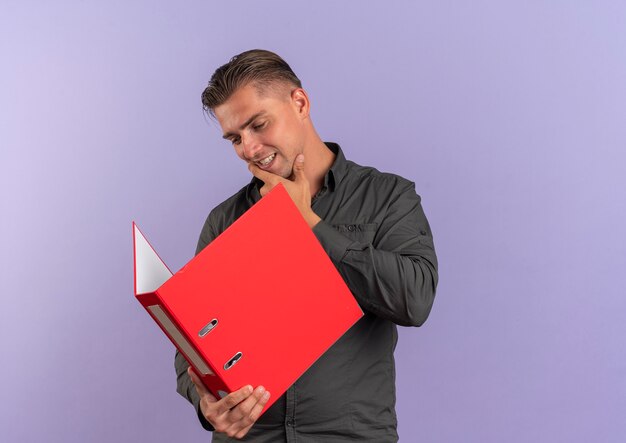 Jeune homme beau blond heureux tient et regarde le dossier de fichiers isolé sur l'espace violet avec copie espace
