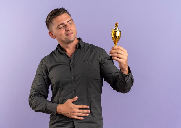 Jeune homme beau blond heureux tient et regarde la tasse isolée sur l'espace violet avec copie espace