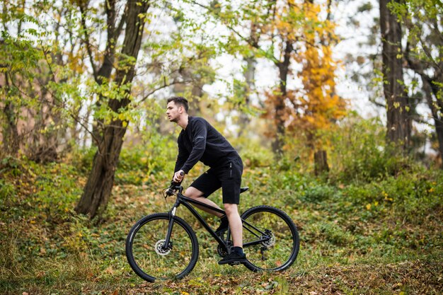 Jeune homme beau sport avec sa formation de vélo dans le parc en automne.