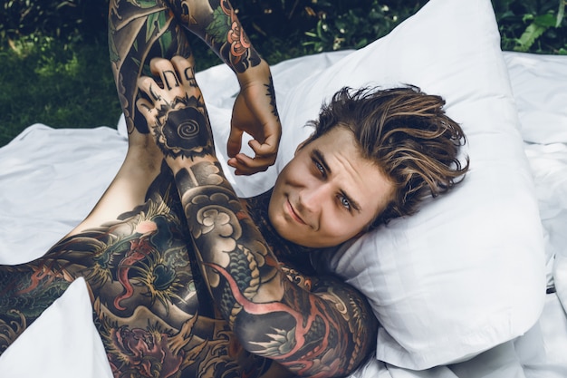 un jeune homme beau tatoué le matin au lit jette les oreillers