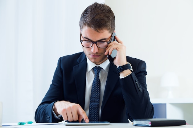 Jeune homme beau travaillant dans son bureau avec un téléphone mobile.