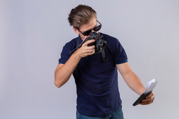 Jeune homme beau voyageur à l'aide de l'appareil photo en prenant des photos de ses billets debout sur fond blanc