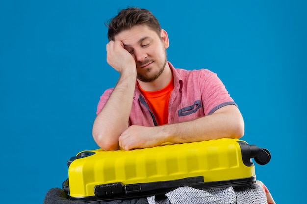 Jeune homme beau voyageur debout avec une valise pleine de vêtements, l'air fatigué