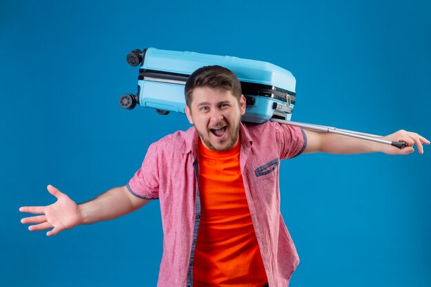 Jeune homme beau voyageur tenant valise fou et fou criant avec une expression de colère