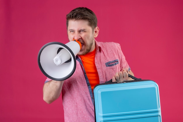 Jeune homme beau voyageur tenant valise et mégaphone en criant à elle