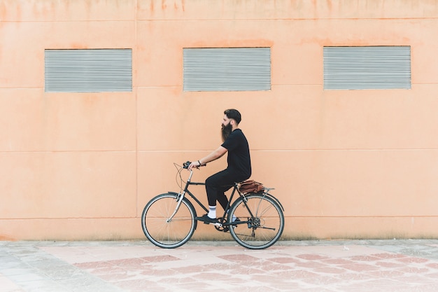 Jeune homme à bicyclette devant le mur beige