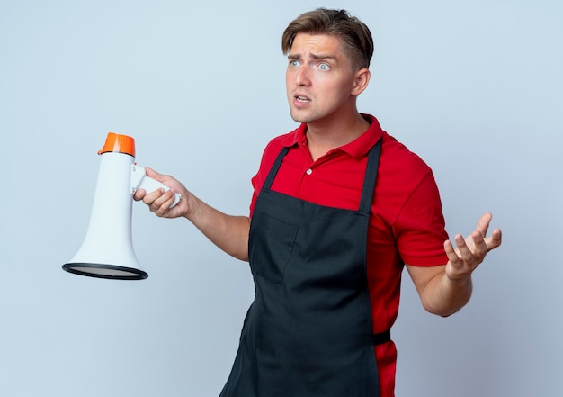 Photo gratuite jeune homme blond anxieux coiffeur en uniforme détient haut-parleur isolé sur un espace blanc avec copie espace