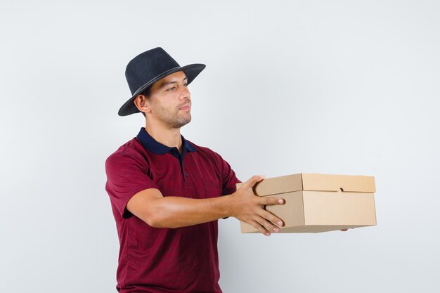 Jeune homme boîte de remise en chemise rouge, chapeau noir et à la recherche de prêt. vue de face.