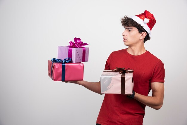 Jeune homme en bonnet de Noel regardant des cadeaux.