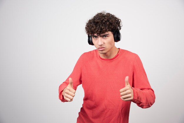 Jeune homme bouclé écoutant la chanson et donnant des pouces vers le haut.