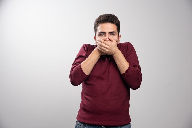 Un jeune homme brune couvrant sa bouche et posant.