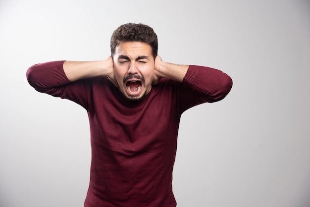 Un jeune homme brune couvrant ses oreilles et posant.