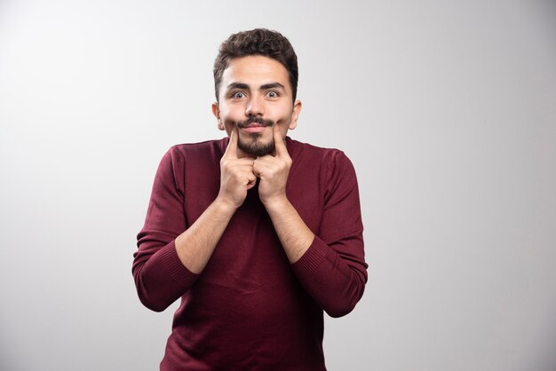 Un jeune homme brune resserre son sourire sur un mur gris