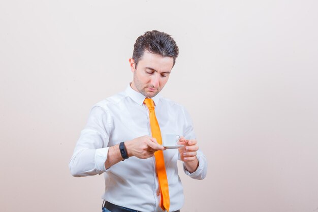 Jeune homme buvant du café turc en chemise blanche, cravate et regardant attentivement