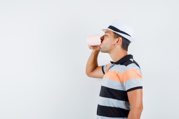 Jeune homme buvant une tasse de thé en t-shirt et chapeau et à ravi