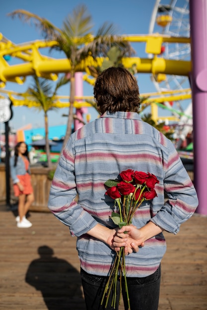 Jeune homme cachant un bouquet de fleurs pour sa petite amie lors d'un rendez-vous au parc d'attractions