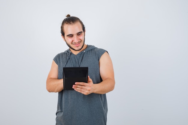 Jeune homme à capuche comptant sur la calculatrice et à la vue réfléchie, de face.