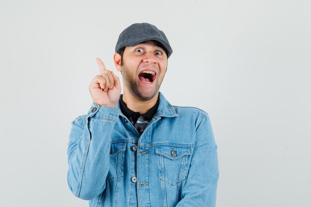 Jeune homme en casquette, t-shirt, veste pointant vers le coin supérieur gauche et l'air heureux