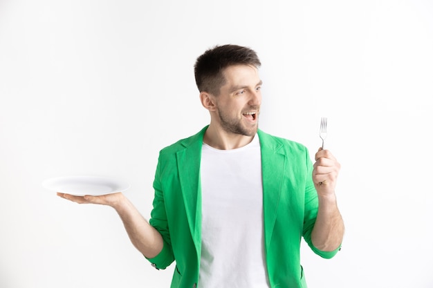 Jeune homme caucasien attrayant souriant tenant un plat vide et une fourchette isolé sur fond gris