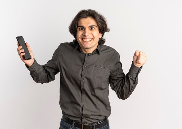 Jeune homme caucasien beau joyeux tient le téléphone et garde le poing isolé sur fond blanc avec espace de copie