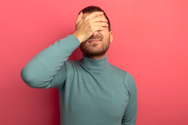 Jeune homme caucasien couvrant les yeux avec la main isolé sur fond cramoisi avec espace copie