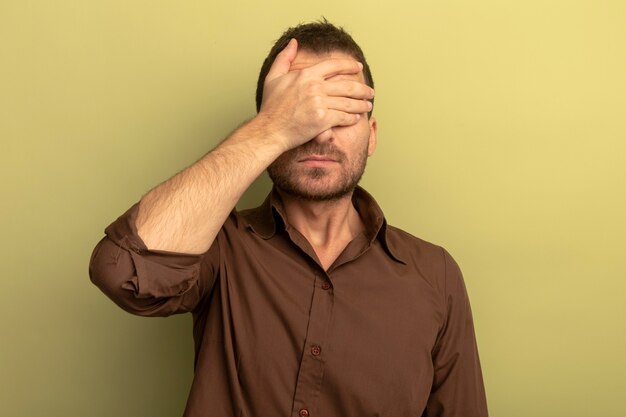 Jeune homme caucasien couvrant les yeux avec la main isolé sur fond vert olive avec espace copie