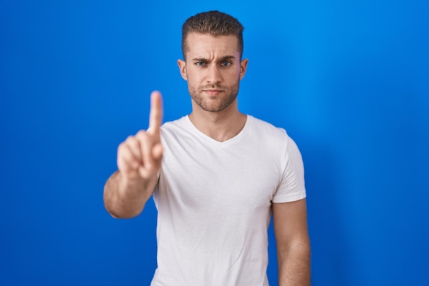 Photo gratuite jeune homme caucasien debout sur fond bleu pointant avec le doigt vers le haut et expression de colère ne montrant aucun geste