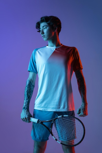 Jeune Homme Caucasien Jouant Au Tennis Isolé Sur Fond De Studio Bleu Violet Dans Le Concept D'action Et De Mouvement Au Néon Photo Premium