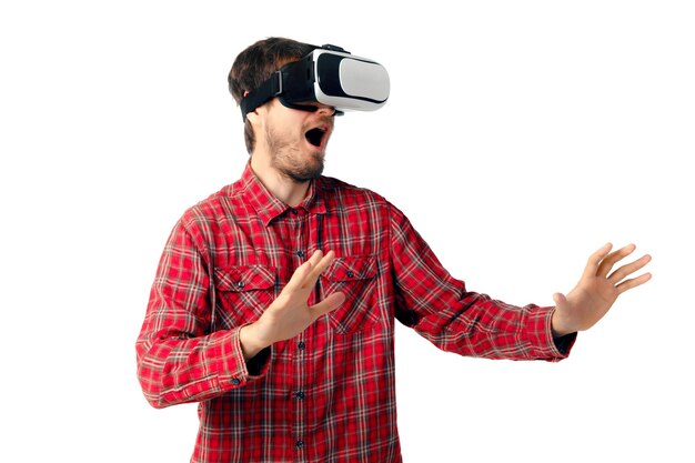 Jeune homme caucasien jouant émotionnellement, à l'aide d'un casque de réalité virtuelle isolé sur le mur blanc du studio. Concept de technologies modernes, gadgets, technologie, émotions humaines, publicité. Espace de copie. AR, VR.