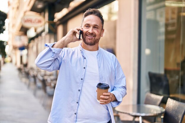 Jeune homme caucasien parlant sur le smartphone en buvant du café à la terrasse du café