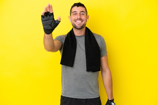 Jeune homme caucasien de sport isolé sur fond jaune saluant avec la main avec une expression heureuse