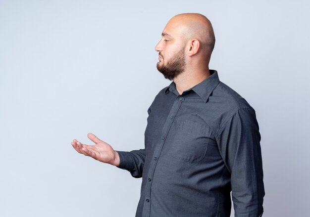 Jeune homme de centre d'appels chauve debout en vue de profil montrant la main vide et à la droite isolé sur fond blanc