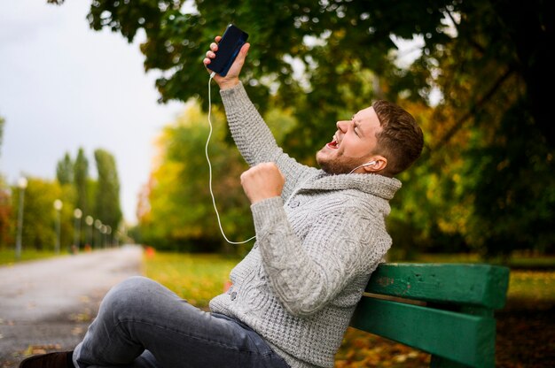 Jeune homme chantant sur un banc dans le parc