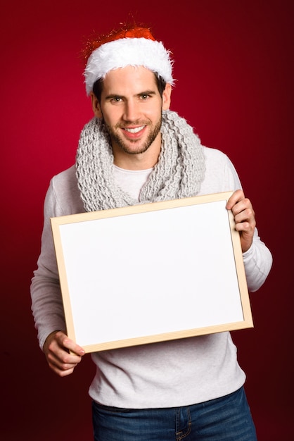 Jeune homme avec un chapeau de Santa tenant un tableau blanc