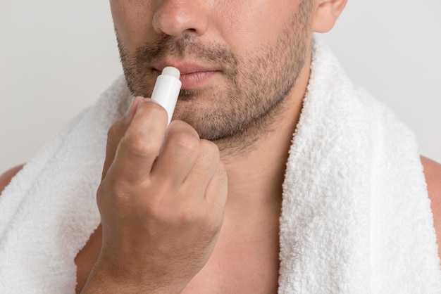 Photo gratuite jeune homme chaume avec une serviette blanche appliquant un baume sur les lèvres