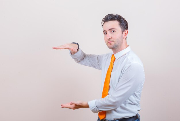 Jeune homme en chemise blanche, cravate montrant le signe de la taille et l'air confiant