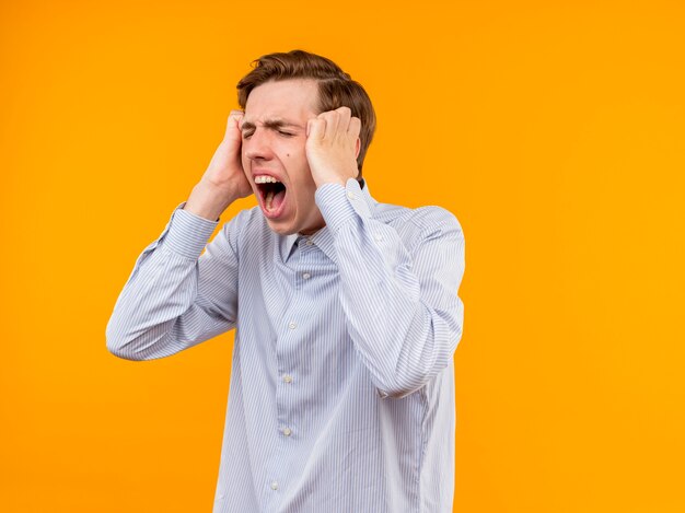 Jeune homme en chemise blanche frustré en colère avec une expression agressive debout sur un mur orange