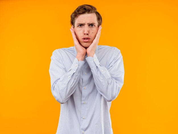 Jeune homme en chemise blanche à inquiet debout sur un mur orange